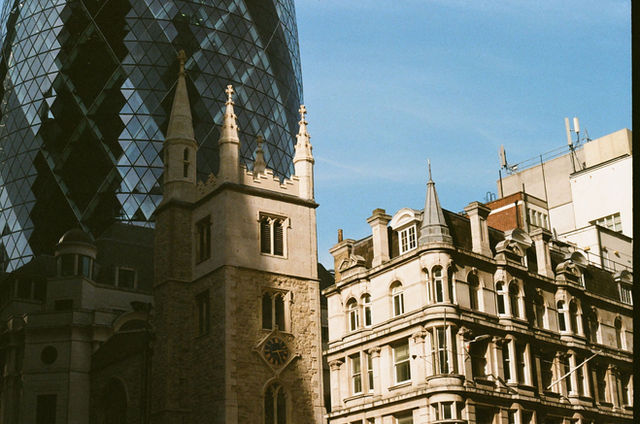 The Gherkin and historic buildings in London under a bright blue sky.