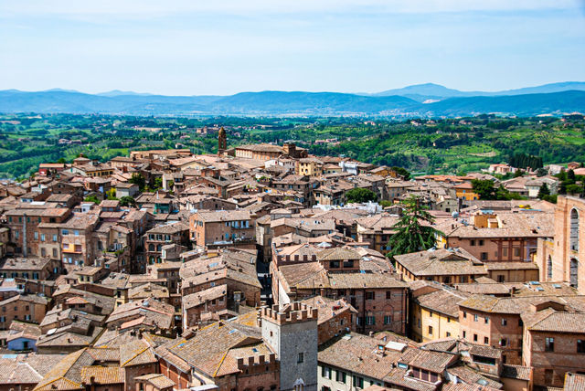 Discover the charming rooftops of Siena, Tuscany, captured from above with lush green hills in the backdrop.