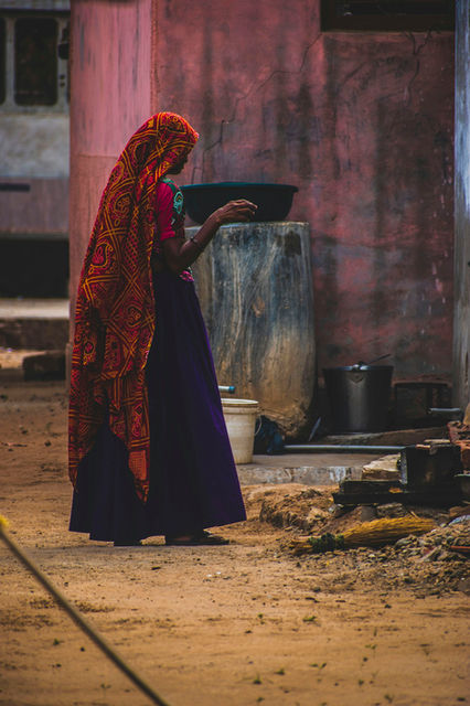 A woman in red and indigo beside a weathered post