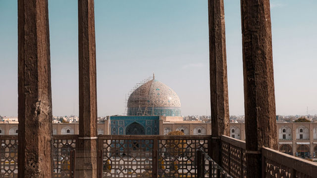Beautiful capture of the Shah Mosque in Isfahan, featuring intricate architecture behind wooden pillars.