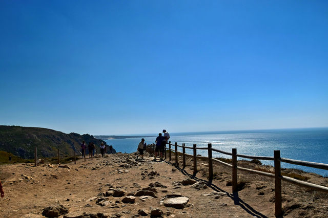 People walk along a coastal path overlooking the ocean.