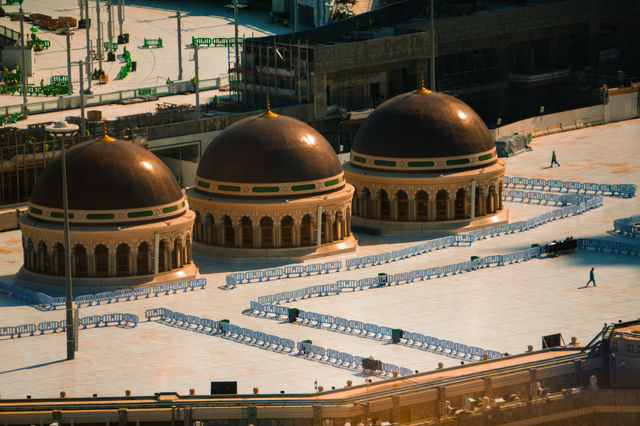 Three prominent domes stand over a large, white mosque courtyard.