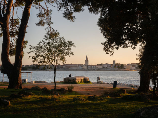 Idyllic sunset view of Poreč, Croatia with trees framing the tranquil coastline and distant townscape.