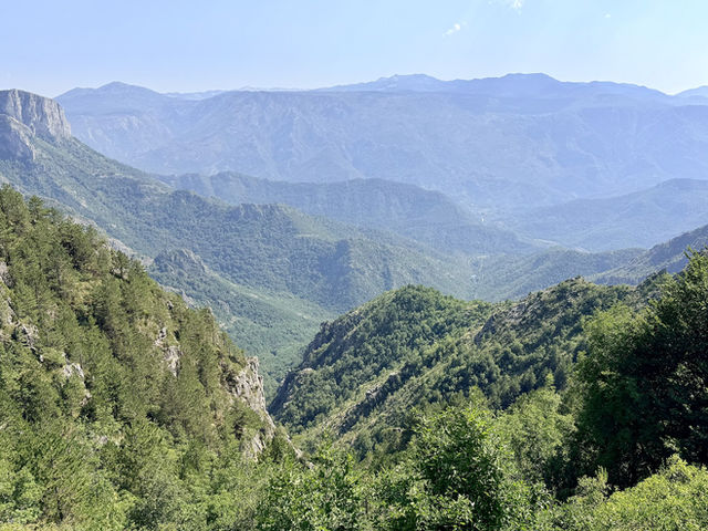 Layered ridges of the Albanian mountains above a deep wooded valley, pale limestone cliffs on the left