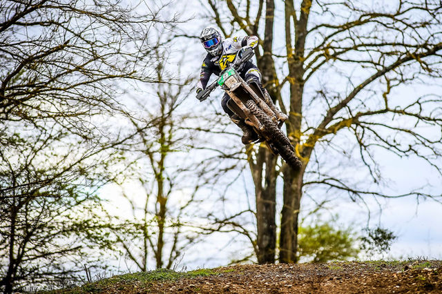 Motocross rider performs an impressive jump amidst the trees in Blois, France.