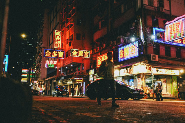 A person walks across a vibrant city street at night.