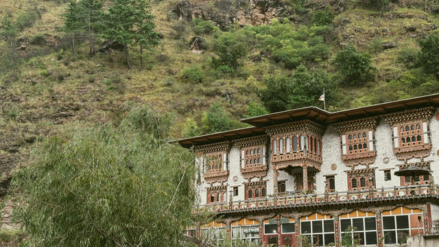 A beautifully detailed traditional building stands against a green hillside in Thimphu, Bhutan, showcasing the intricate woodwork and vibrant patterns that define Bhutanese architecture.