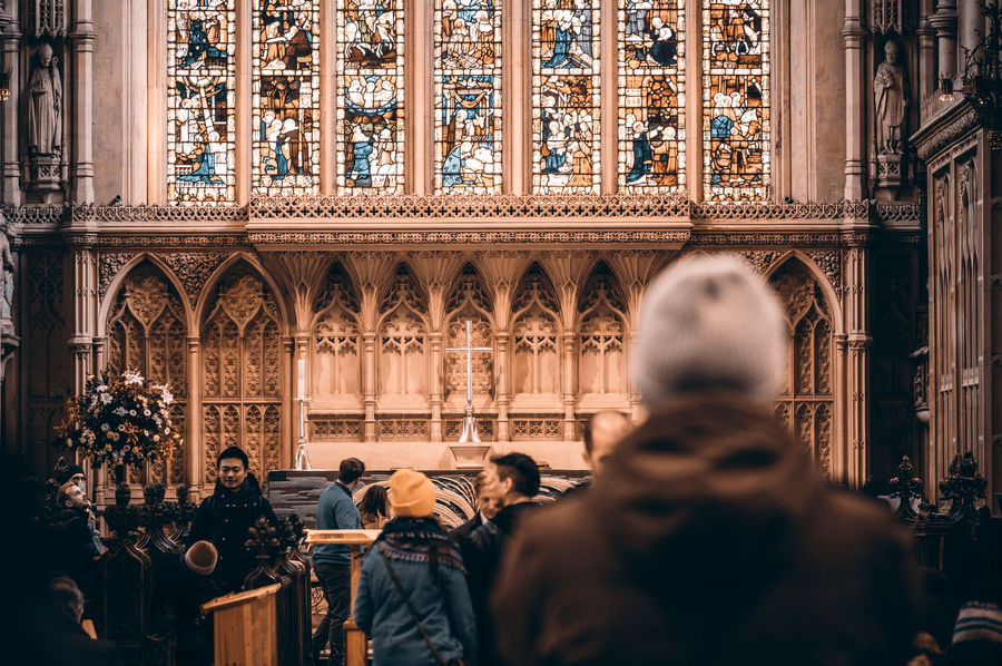 A group of people inside a majestic church in Bath, England, with beautiful stained glass windows.