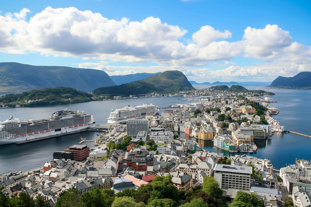 A spectacular aerial view of Ålesund, showcasing its iconic Art Nouveau architecture surrounded by fjords and mountains. Cruise ships dock in the harbor while the vibrant coastal town stretches across