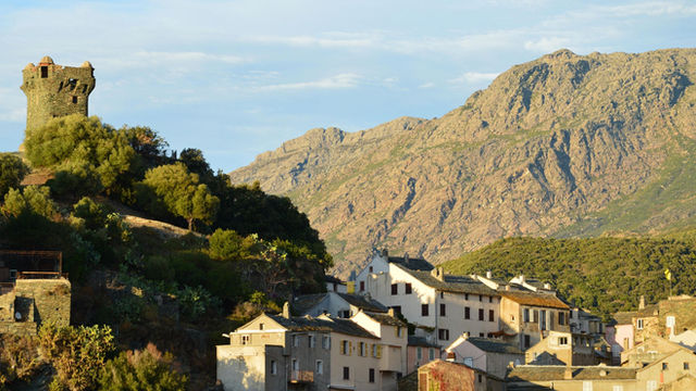 Scenic view of the historic village of Nonza in Corsica with a medieval tower and mountain backdrop.