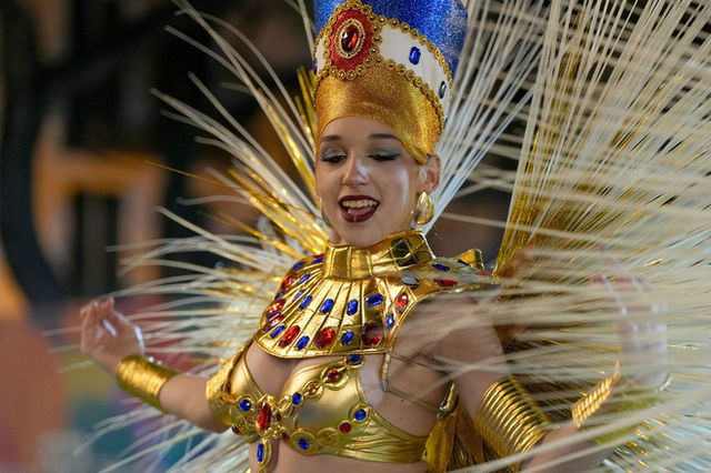 Smiling under an elaborate headpiece, feathers banked behind
