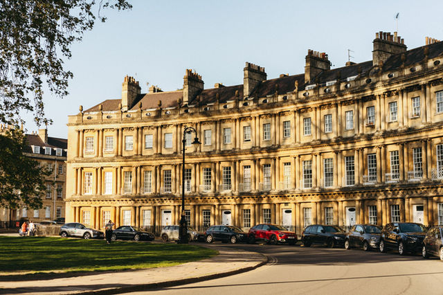 Sunlit Georgian architecture of The Circus in Bath, UK with parked cars and soft shadows.