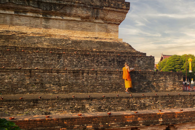 A Buddhist monk lights oil lamps on the ancient temple ruins of Wat Chedi Luang, Chiang Mai, Thailand.