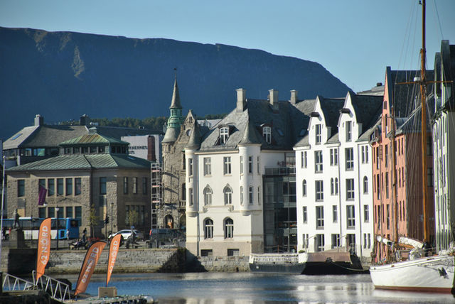 Historic buildings line a waterfront with mountains in the background.