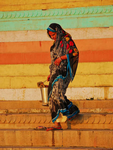 A woman carries a water pail down painted steps