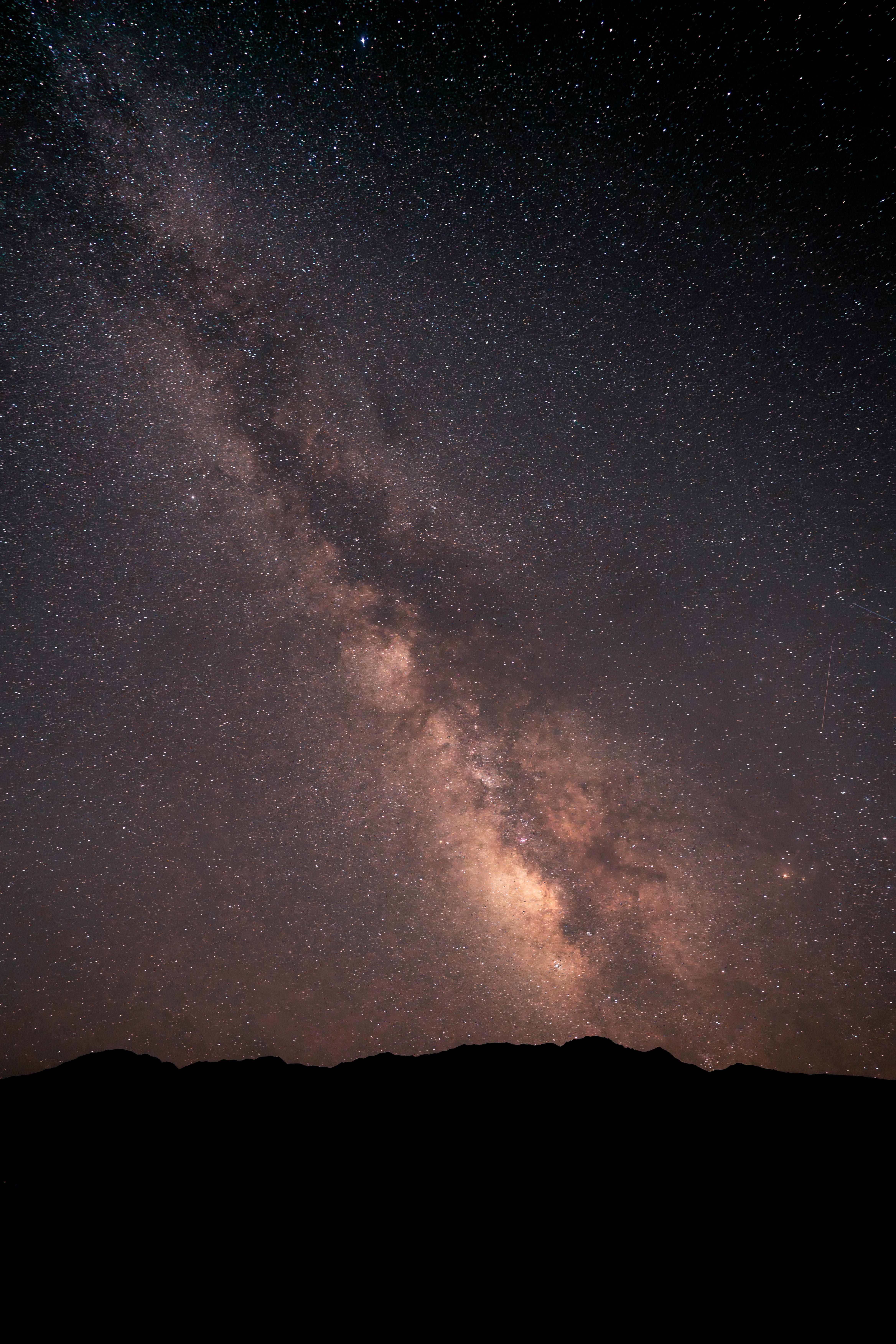 A dark, jagged mountain ridge runs along the bottom edge. Above it, a dense river of stars.