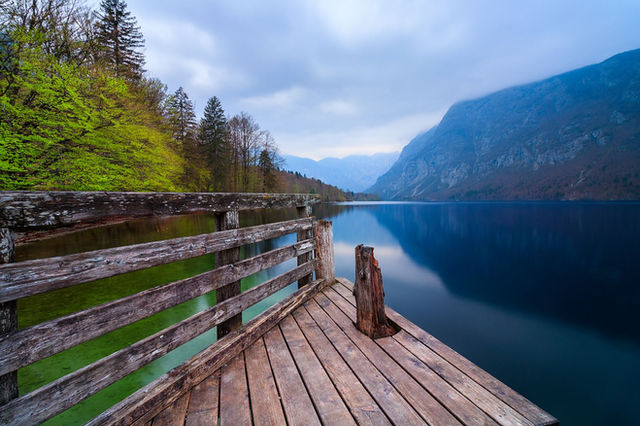Serene wooden pier overlooking Lake Bohinj, surrounded by mountains and lush forest in Slovenia.