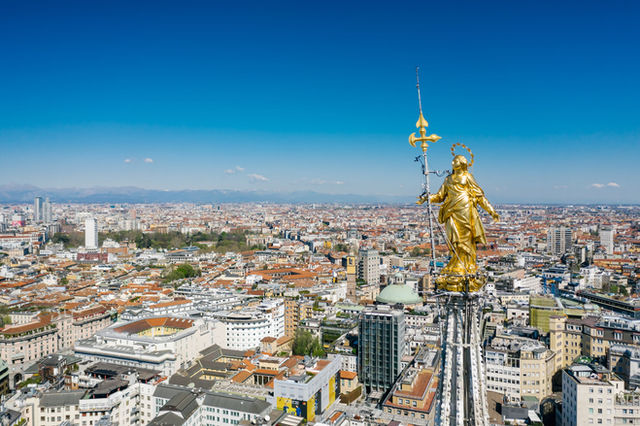 Stunning aerial view of Milan skyline with the iconic golden Madonnina statue under a clear blue sky.