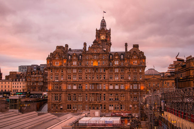 Stunning view of the Edinburgh's Balmoral Hotel at sunset with golden light and cloudy skies.