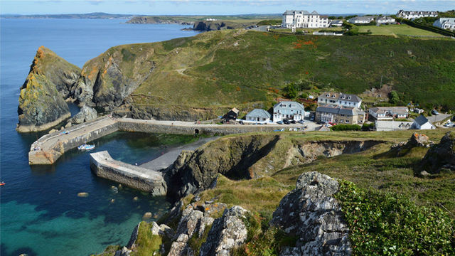 Aerial view of Mullion Cove Harbor with dramatic cliffs and ocean in Cornwall, UK.