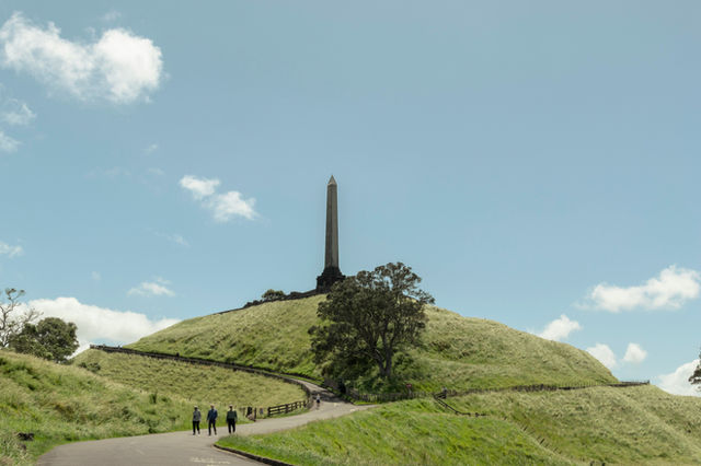 Obelisk on a green hill, winding path, and blue sky.