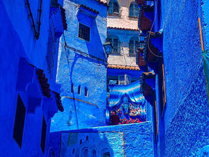 A narrow alleyway in Chefchaouen, Morocco, showcases vibrant blue walls under the bright daylight