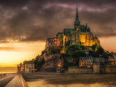 A breathtaking view of Mont Saint-Michel illuminated against the dramatic backdrop of a sunset sky, highlighting its historic grandeur and maritime setting.