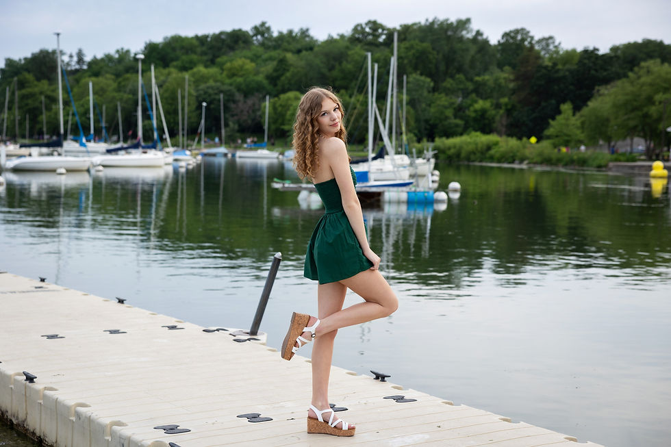 senior portrait in Minneapolis, Minnesota at Lake Harriet - she's wearing a green romper and their are sail boats on the lake in the background