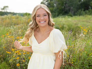 beatuiful senior portrait of a girl laughing with a natural expression during her senior portrait session wearing a yellow shirt in a green, floral meadow