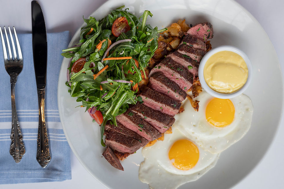 Steak and eggs served with a fresh green salad on a white plate. Mayo in a small cup. Fork and knife on a blue napkin.
