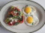 Avocado toast topped with sun-dried tomatoes, feta and herbs beside two sunny-side-up eggs on a white plate.