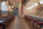 Empty stylish bar and restaurant with red stools, brown booths, hanging globe lights, and an EXIT sign in a warm modern interior.