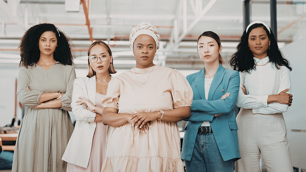 Five women stand confidently with arms crossed in a modern office. They wear varied professional attire in neutral and pastel colors.
