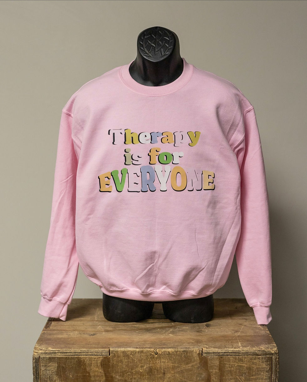 Pink sweatshirt with colourful writing on it that says Therapy is for EVERYONE. 