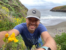 David Lowry smiling with a monkeyflower by the ocean.