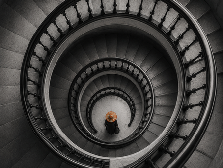 Spiral staircase viewed from above with a salesperson standing at the centre, illustrating how sales training, coaching and capability development can improve performance while an underlying sales pattern remains unresolved.