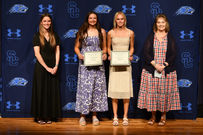 Four women posing with scholarship awards on stage.