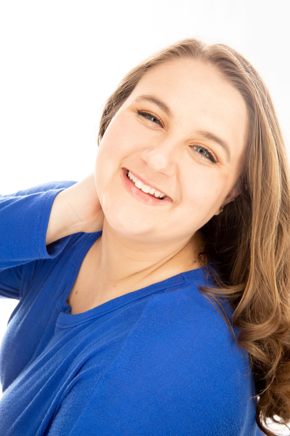 Camri in a blue shirt smiles with her hand on her neck