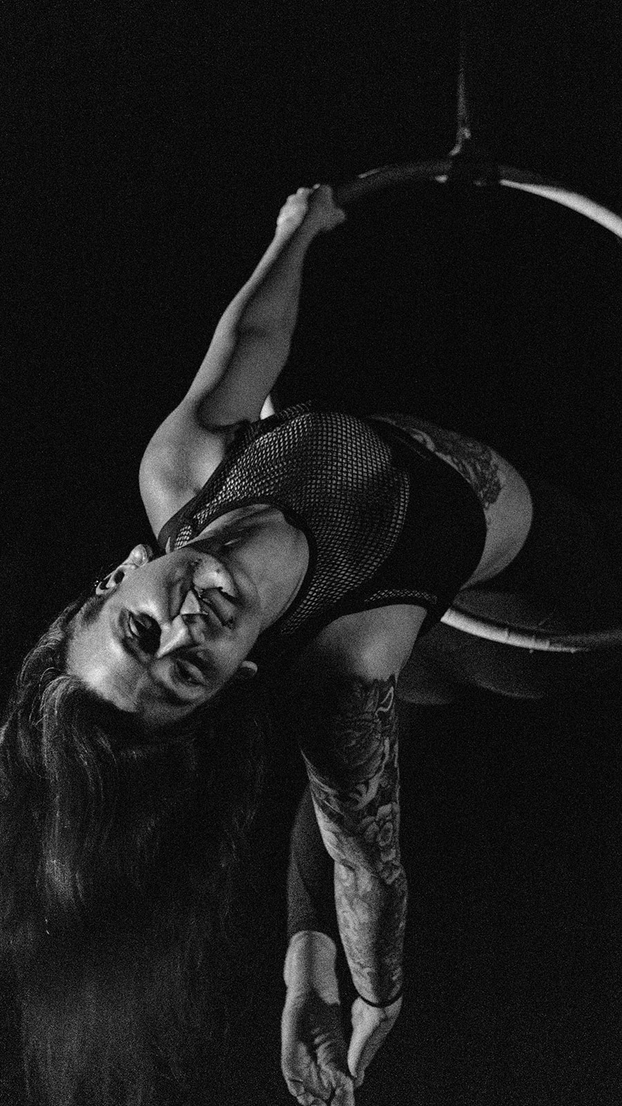 A stunning aerialist performing gracefully on a Lyra in an outdoor setting.
