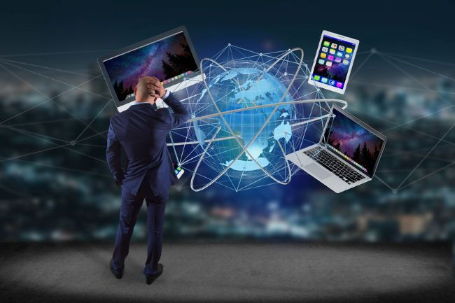 A man in a suit stands before a digital globe, surrounded by floating laptops and a tablet, in a starry night setting, pondering technology.