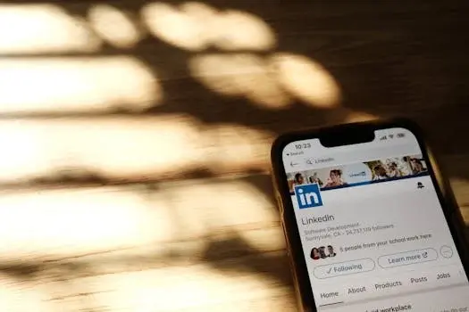 Smartphone displaying LinkedIn app on a wooden surface. Soft sunlight creates shadow patterns in the background, adding a warm mood.