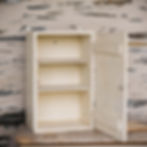 Ancienne armoire à pharmacie murale en bois patiné blanc avec croix rouge, porte ouvrante et étagères intérieures, style broc