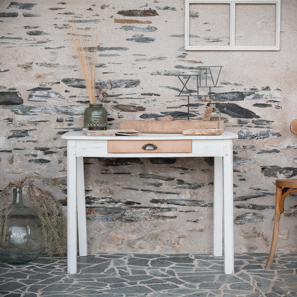 Table console ancienne en bois à patine blanche d’origine avec tiroir central, posée contre un mur en pierre.