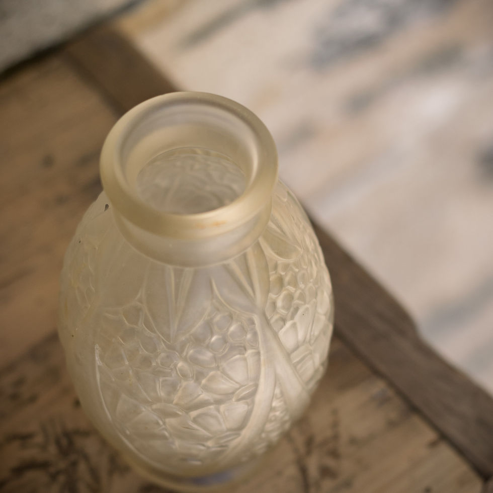 Vase Art déco JOMA en verre moulé dépoli à décor floral en relief posé sur une caisse ancienne en bois.