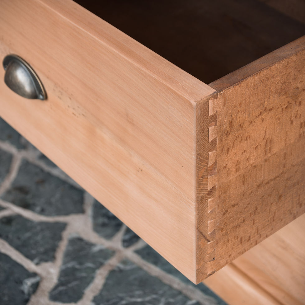 Miniature : Commode basse en merisier massif avec tiroirs et poignées coquille, meuble en bois naturel posé contre un mur en pierre.