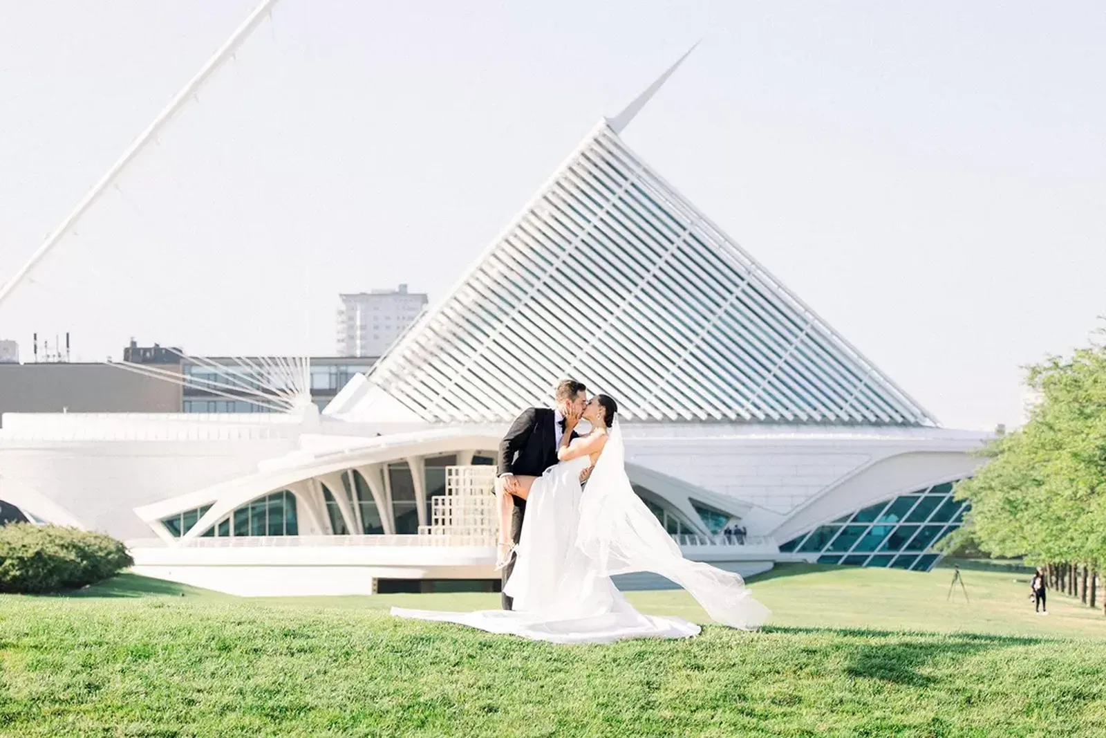 A bride and groom kissing in front of the milwaukee art musuem