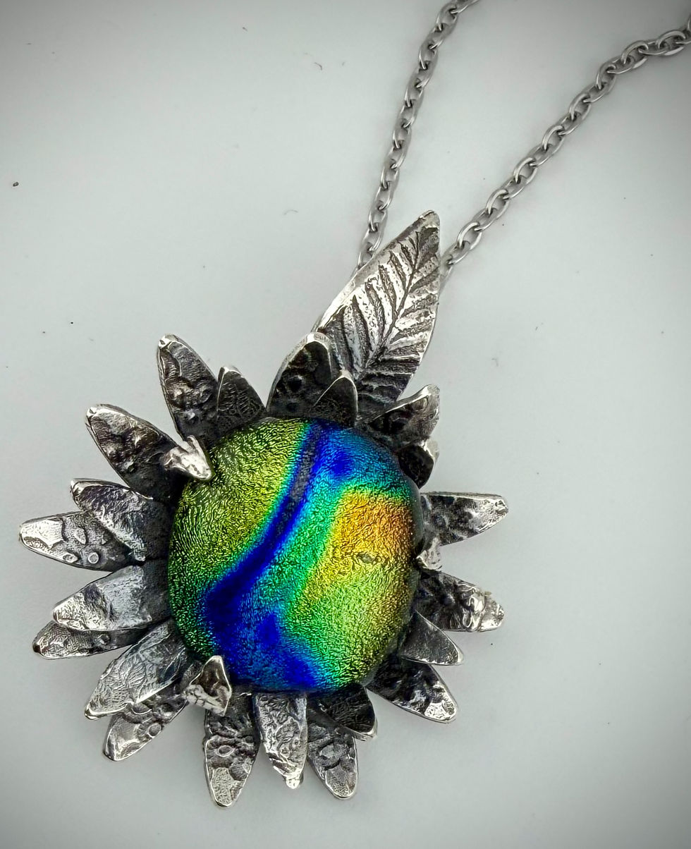 Close-up of dichroic glass cabochon with leaf-shaped silver bail, highlighting iridescent green, blue, and purple hues.