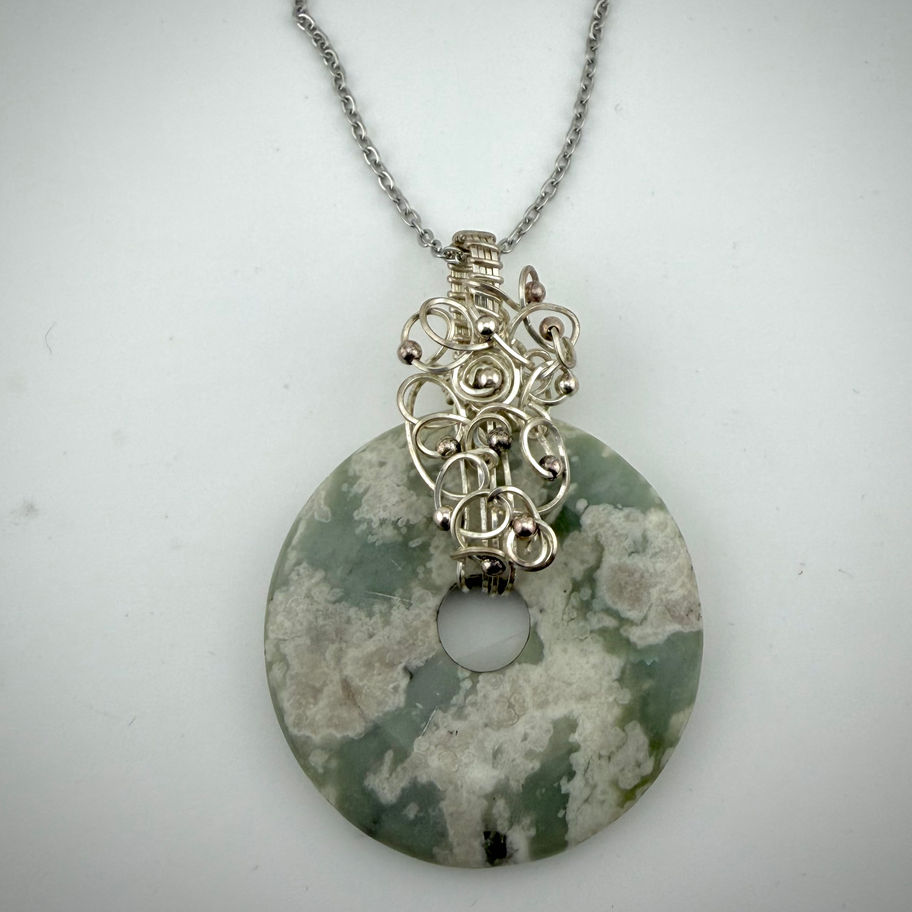 Front view of Curly Flower Agate donut pendant with green and cream stone and intricate silver bail detail