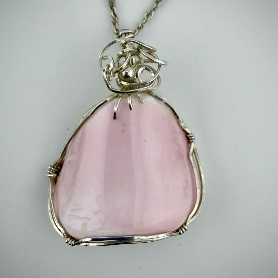 Front view of pink conch shell pendant showing soft blush tones encased in hand-wrapped sterling silver wire.