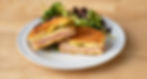 halves of a meat, cheese and pickle panini with side salad
